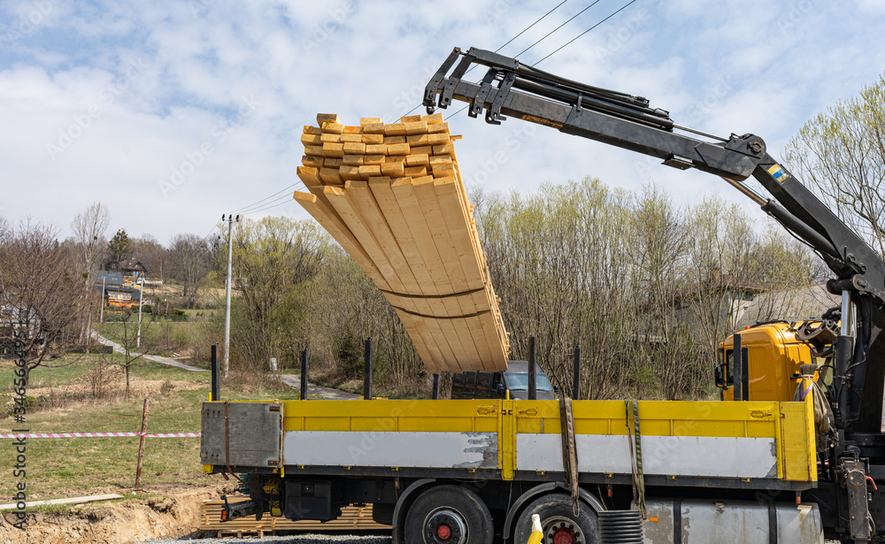 Unloading wooden beams from truck on construction site  for building a house