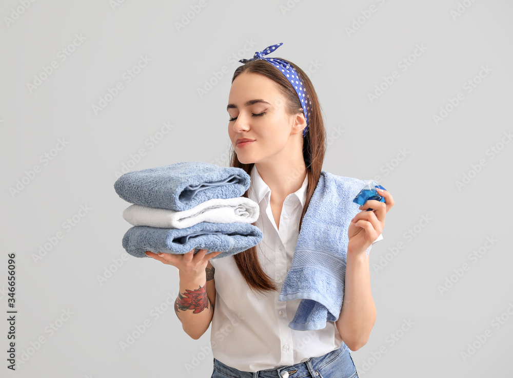 Beautiful young woman with clean towels and detergent on grey background