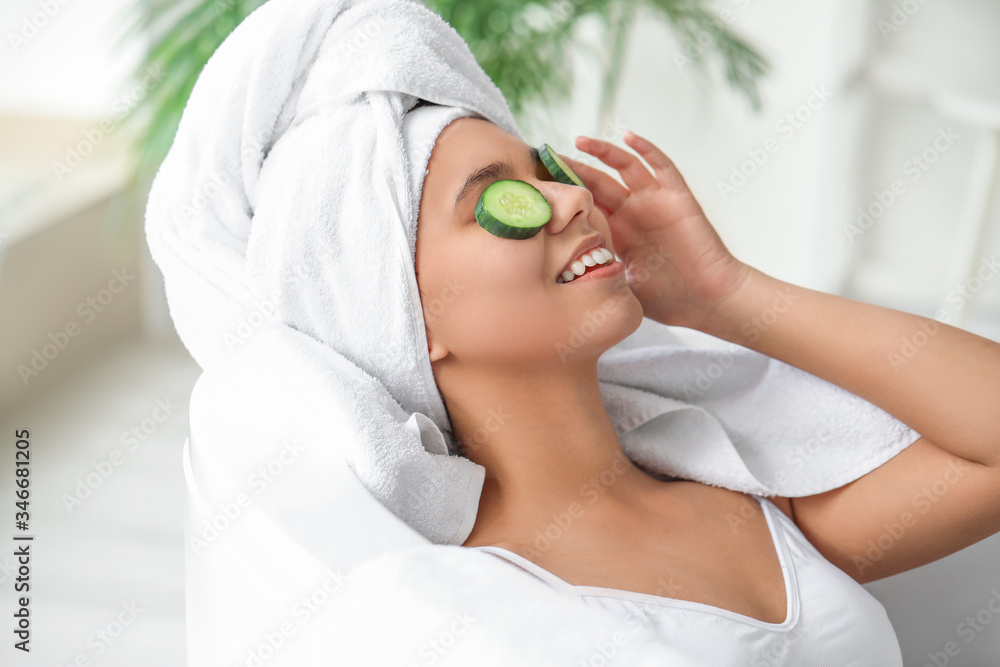 Beautiful young African-American woman with cucumber slices in bathroom