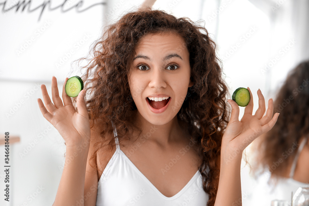 Beautiful young African-American woman with cucumber slices in bathroom