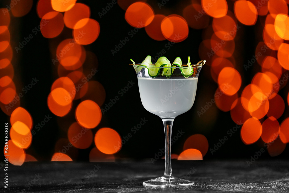 Glass of tasty cucumber martini on dark background with blurred lights