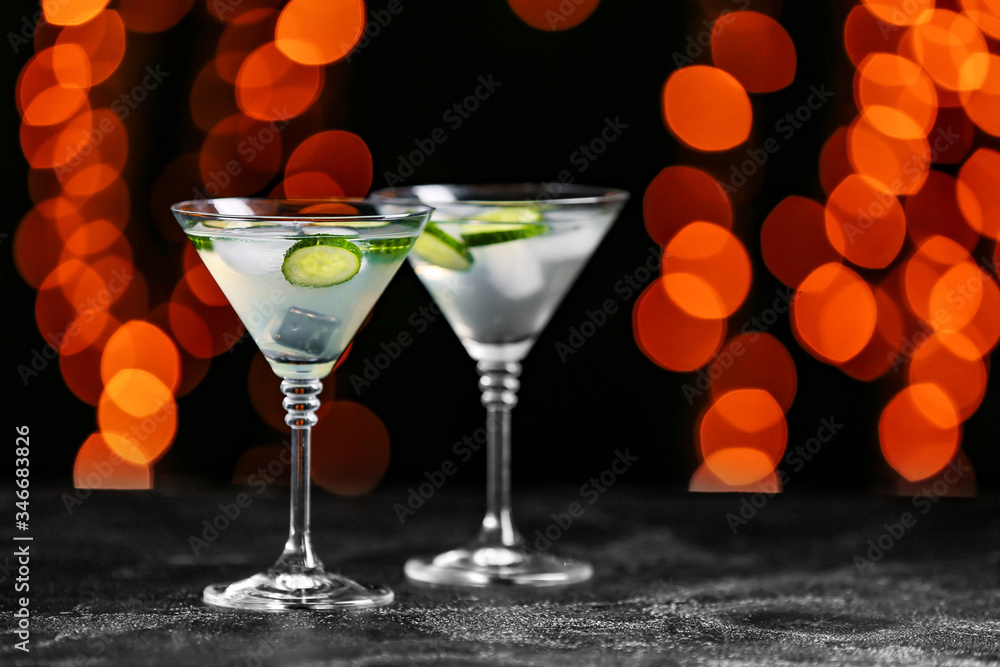 Glasses of tasty cucumber martini on dark background with blurred lights