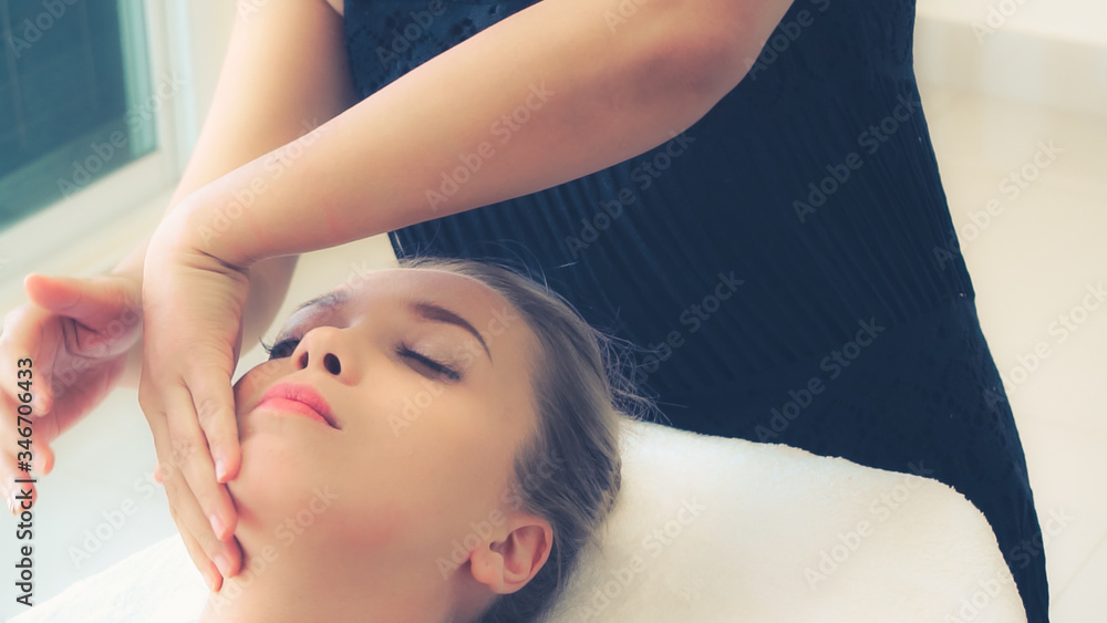 Relaxed woman lying on spa bed for facial and head massage spa treatment by massage therapist in a l