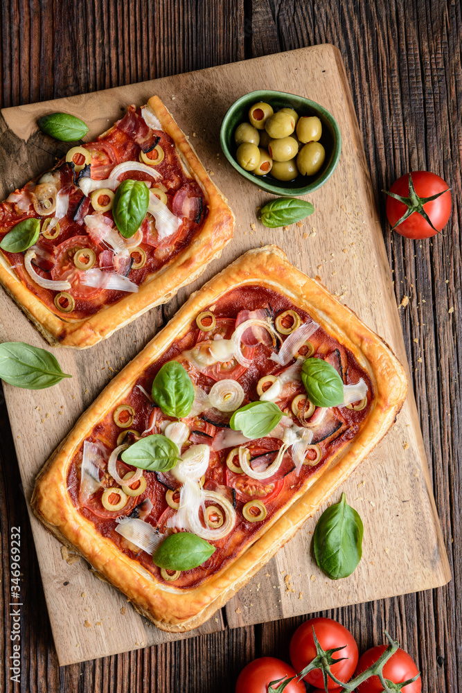 Homemade puff pastry pizza with bacon slices, tomatoes, green olives, cheese and onion, topped with 