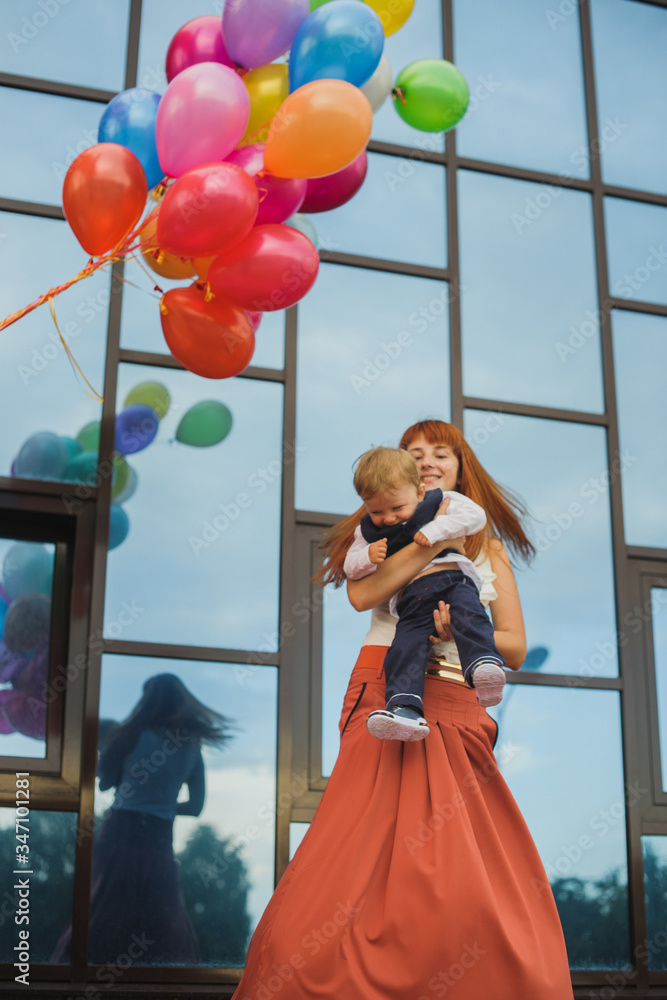 woman holding a baby in her arms, joy and fun, balloons of different colors