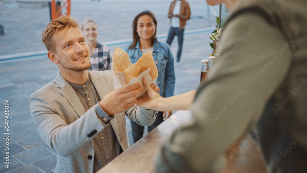 食品车员工向一个穿着西装的快乐年轻人分发新鲜汉堡。街头食品车