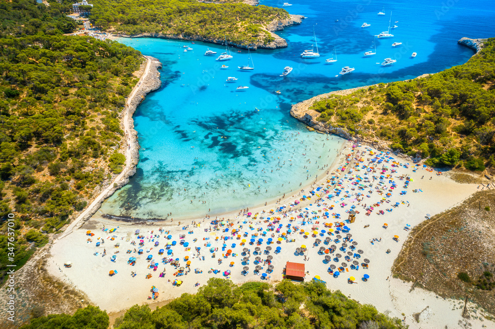 Aerial view of sandy beach with colorful umbrellas, swimming people, boats and yachts in sea bay, gr