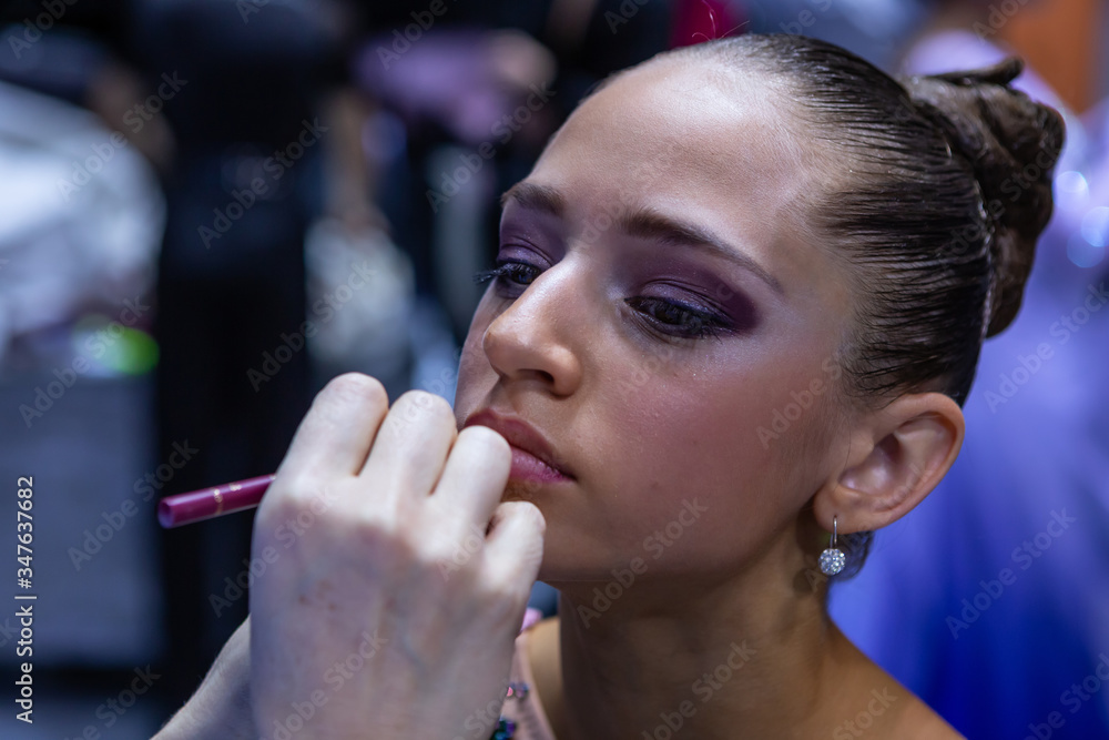 Make-up for ballroom dancer in process. Contouring of lips by bordo pencil. Girl face decoration bef