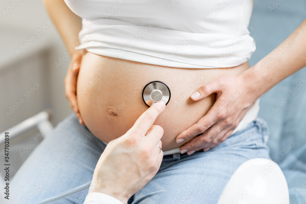 Doctor listening to a pregnant womans belly with a stethoscope during a medical examination, close-