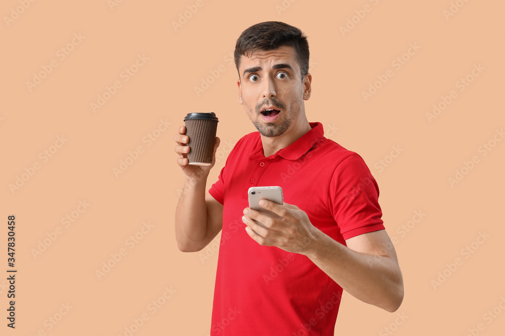 Young man with cup of hot coffee and mobile phone on color background