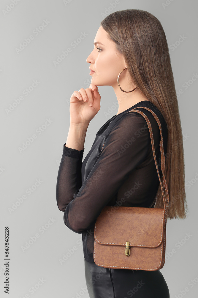 Beautiful woman with stylish bag on grey background