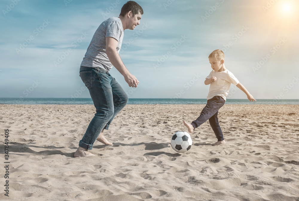 Father and son playing in football on sea coastline beach