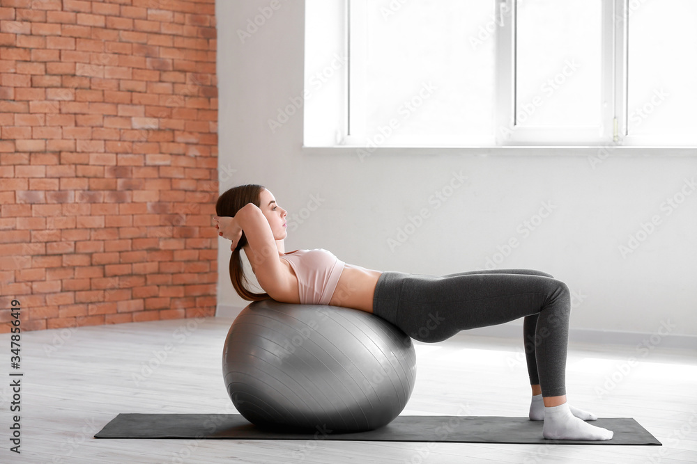 Sporty young woman training with fitball in gym