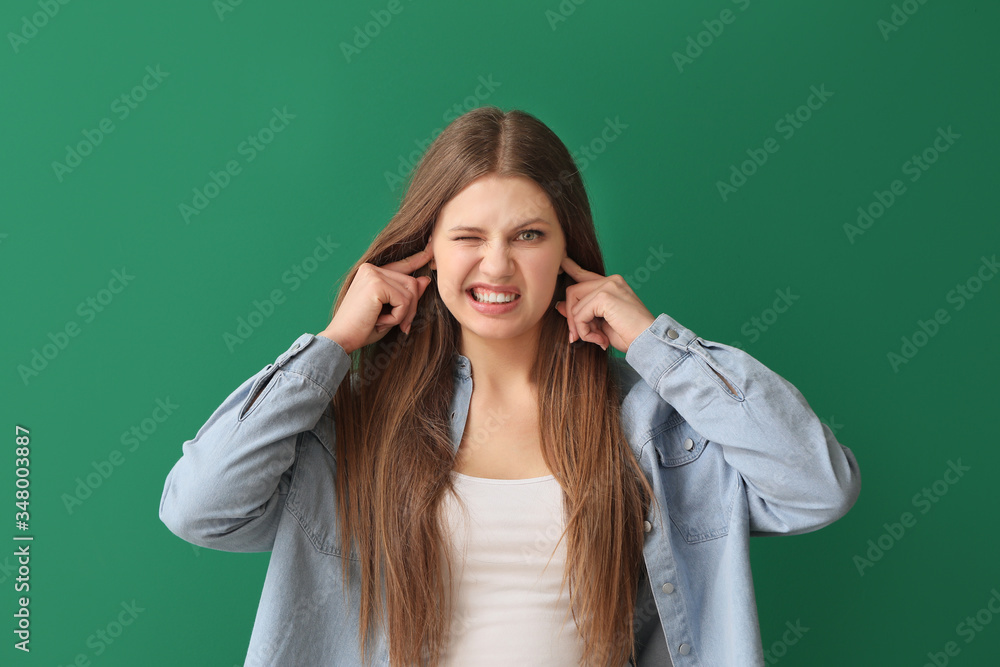 Young woman suffering from loud noise on color background