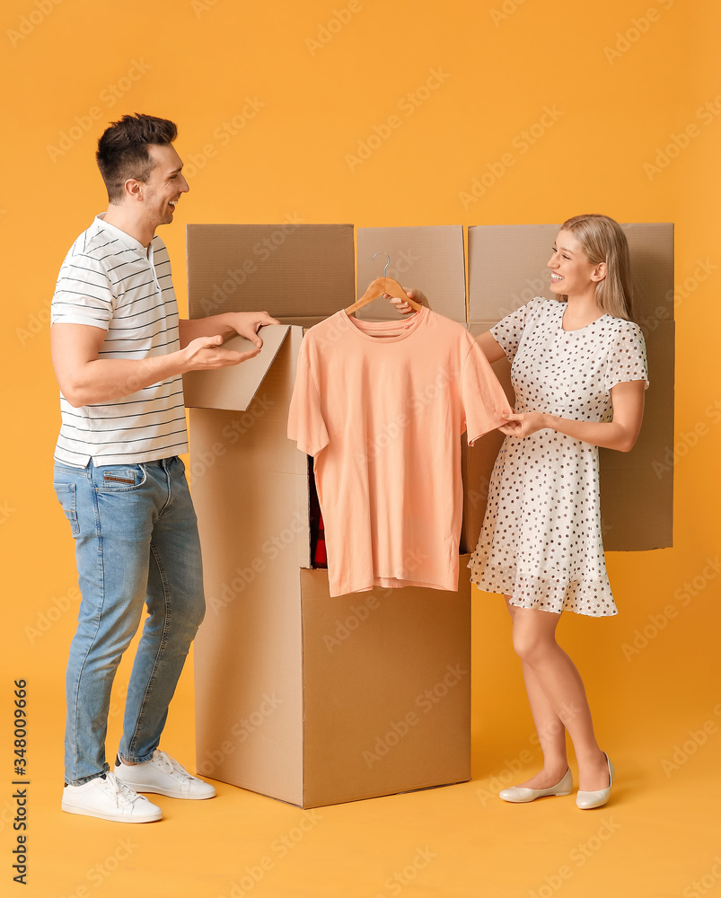 Young couple unpacking clothes on color background