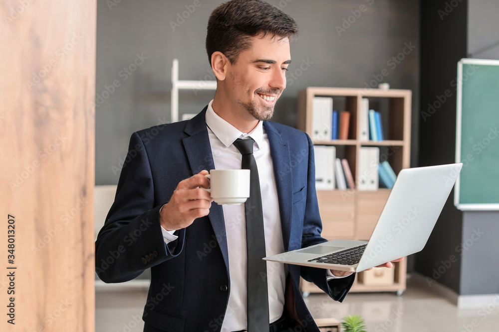 Young businessman with cup of hot coffee and laptop in office