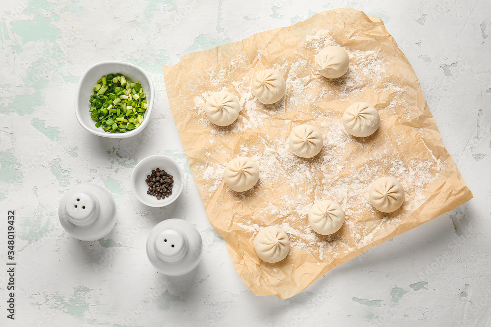 Parchment with raw dumplings on color background