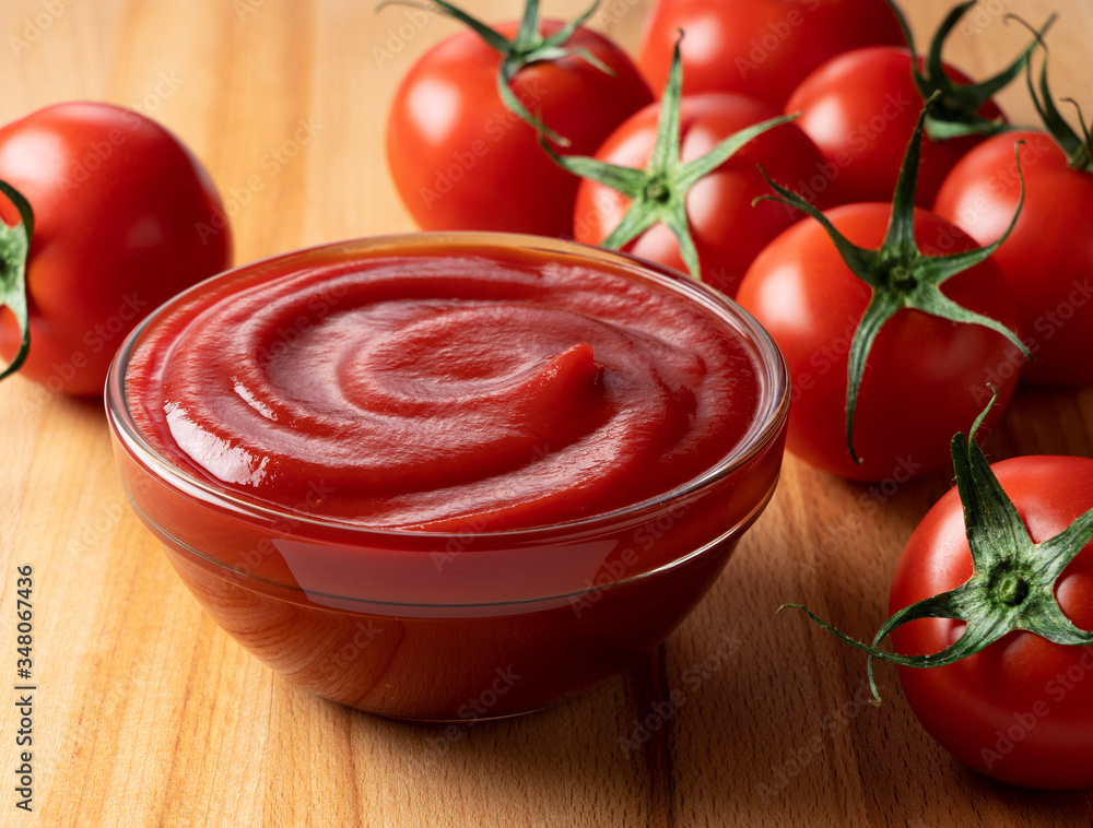 Ketchup placed on a wooden background and multiple tomatoes behind