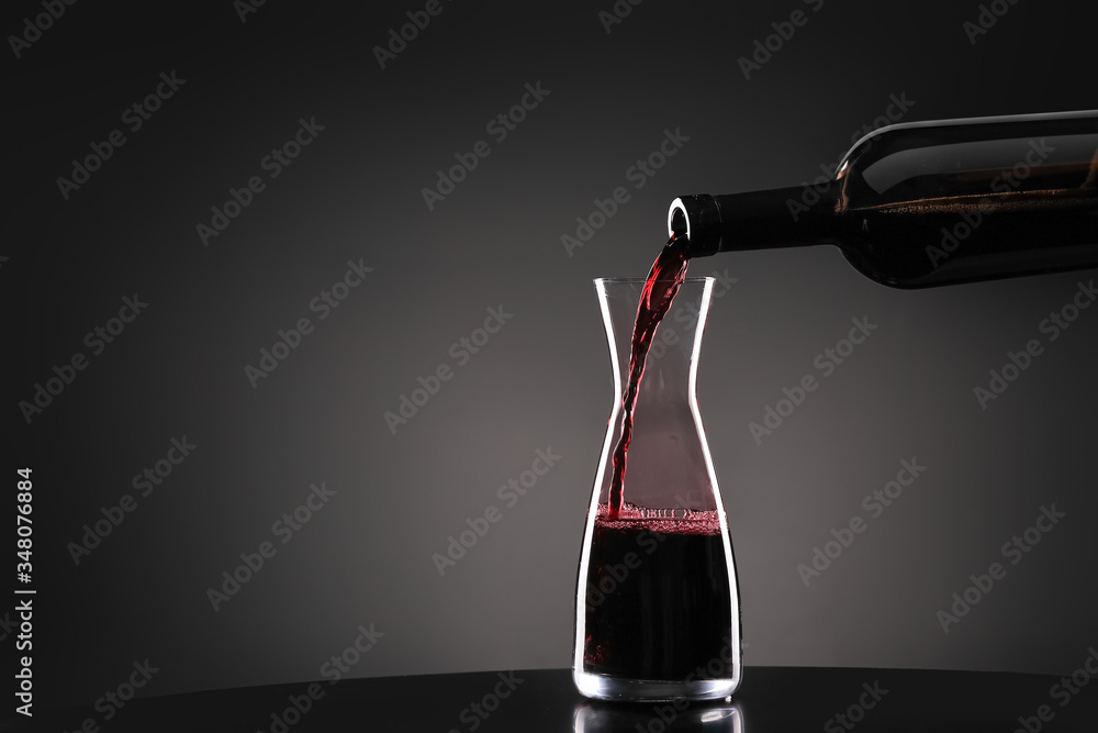 Pouring of tasty wine from bottle into glass on dark background