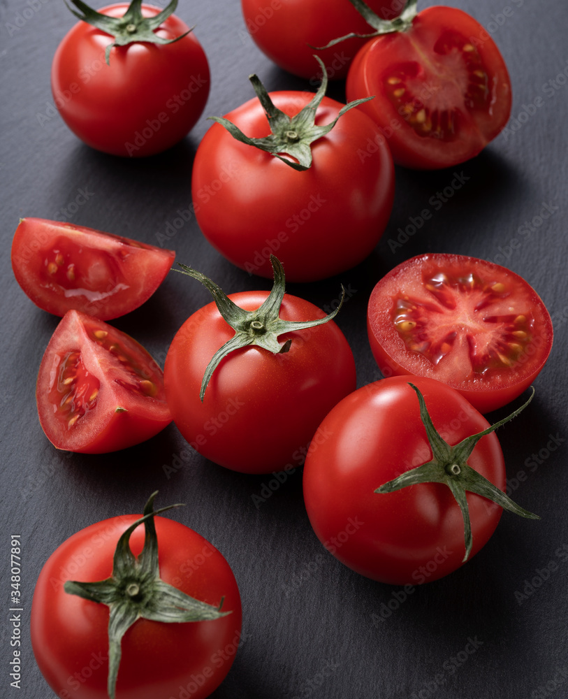 Tomatoes and cut tomatoes placed on black stone background