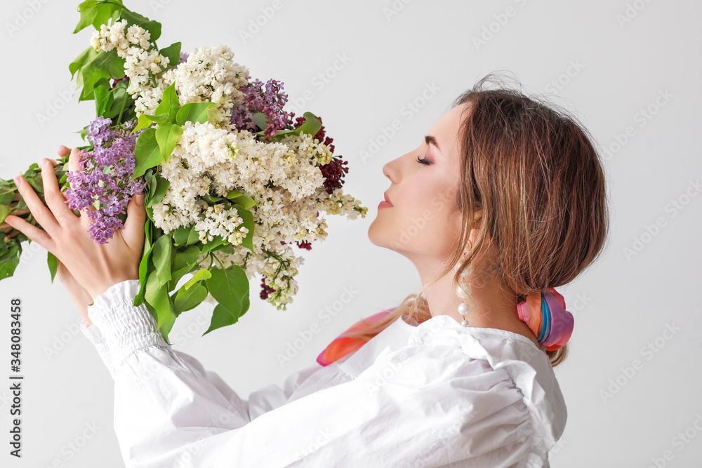 Beautiful young woman with lilac flowers on light background