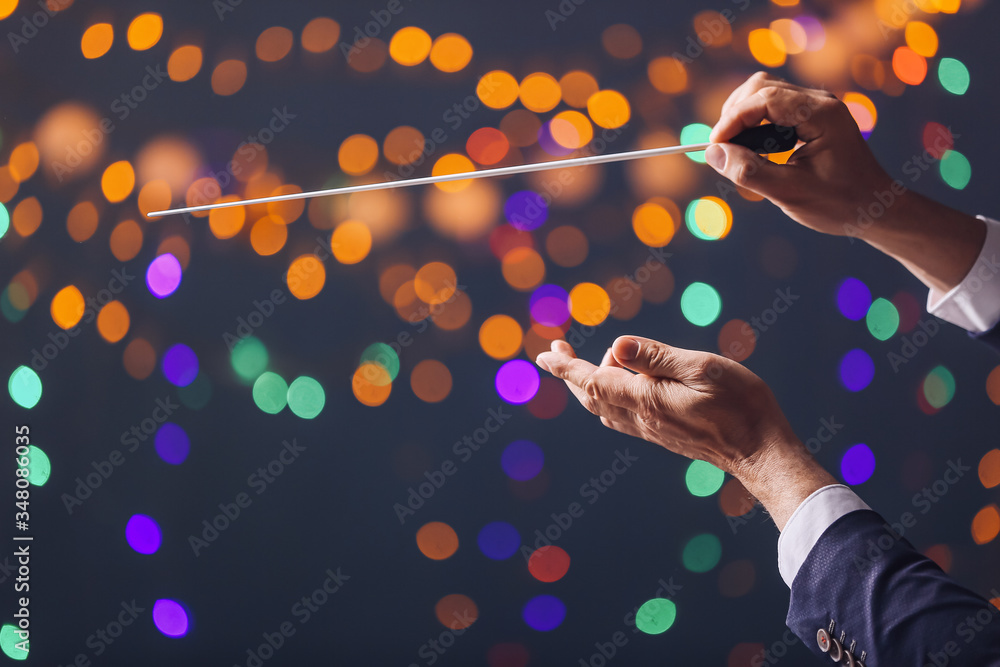 Hands of male conductor on dark background with defocused lights