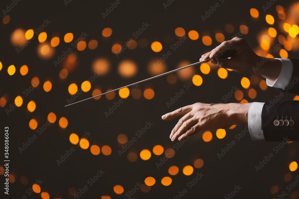 Hands of male conductor on dark background with defocused lights