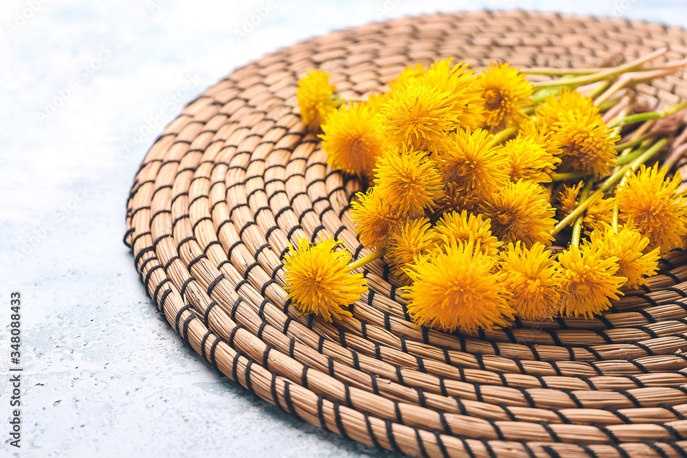 Wicker mat and dandelion flowers on color background