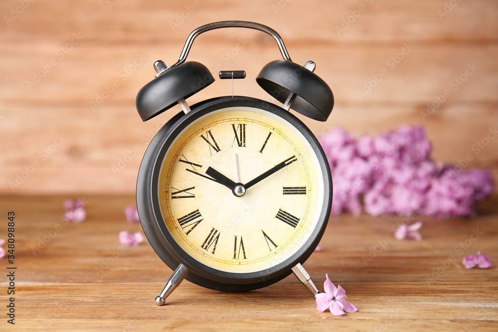 Alarm clock and flowers on wooden table. Spring time