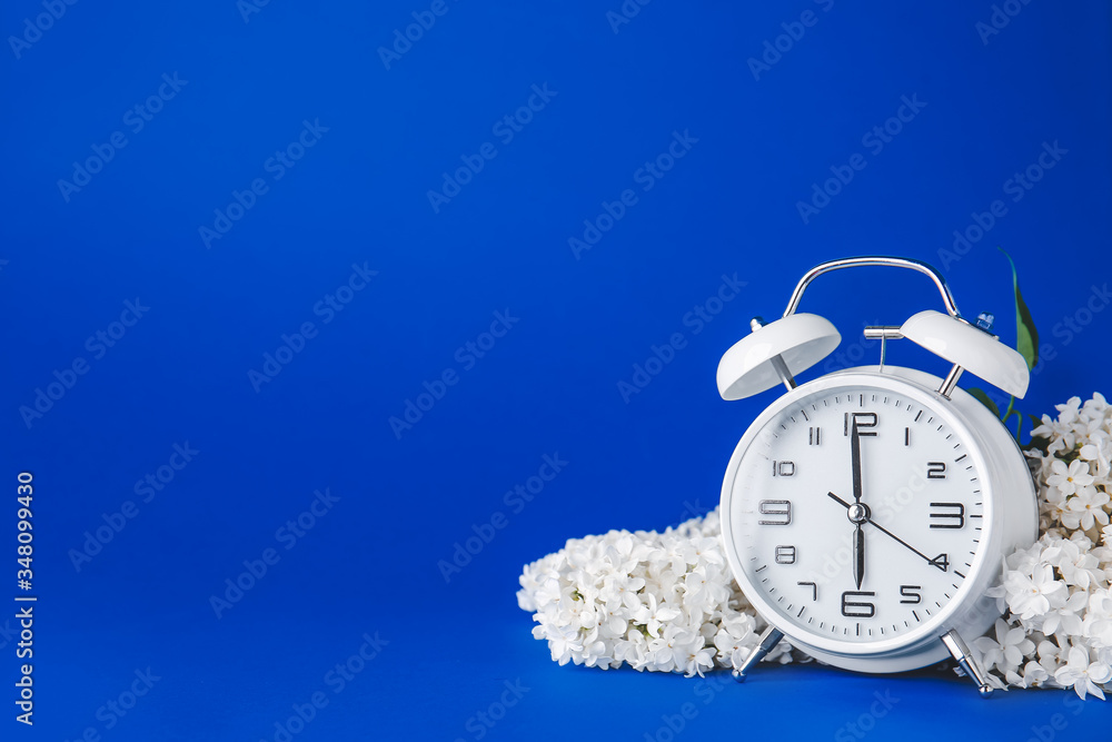 Alarm clock and flowers on color background. Spring time