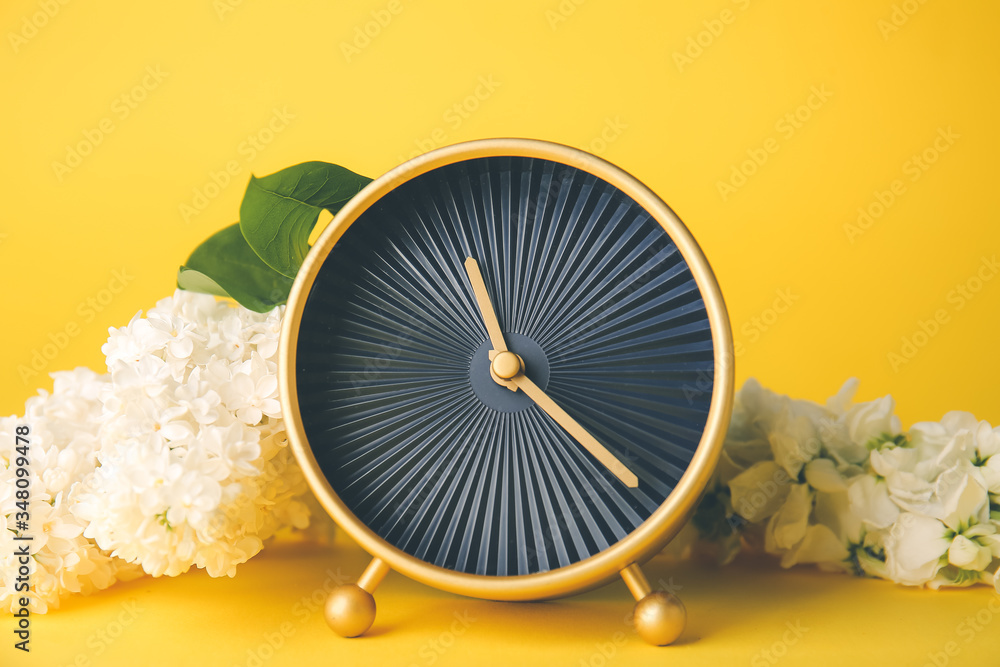 Alarm clock and flowers on color background. Spring time