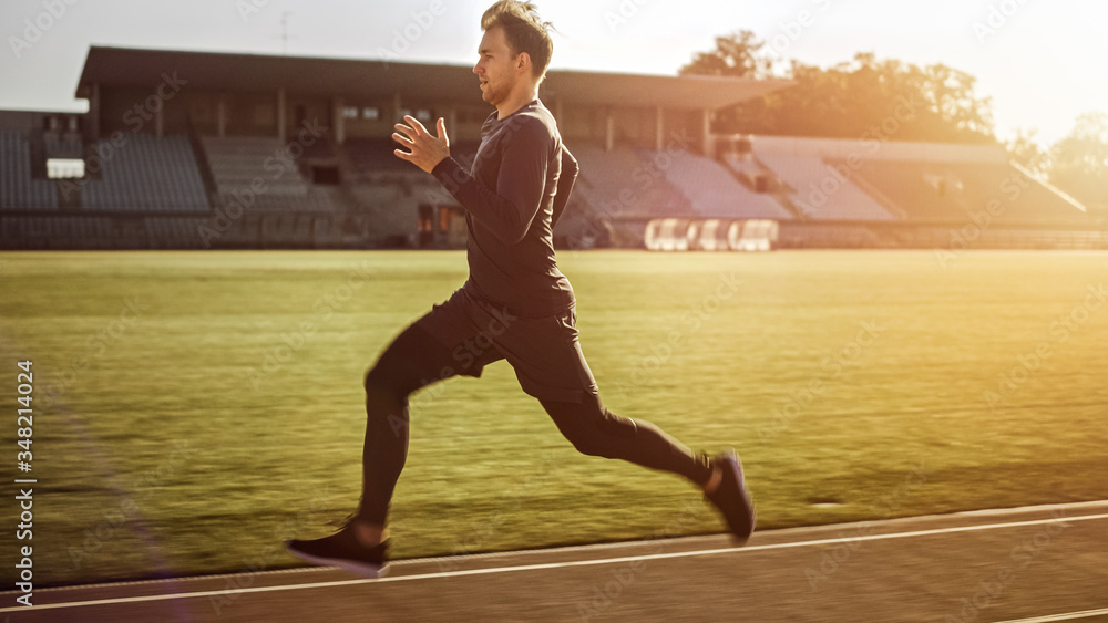 Athletic Fit Man in Grey Shirt and Shorts Jogging in the Stadium. He is Running Fast on a Warm Summe