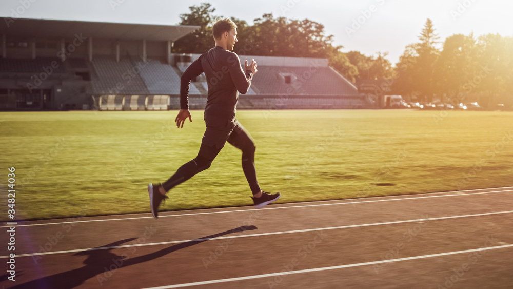 Athletic Fit Man in Grey Shirt and Shorts Jogging in the Stadium. He is Running Fast on a Warm Summe