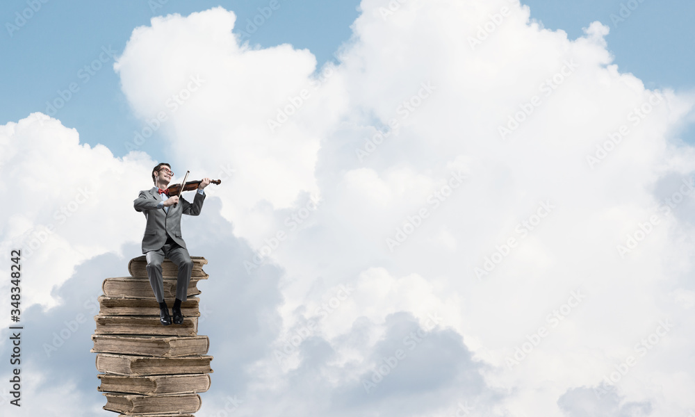 Handsome violinist in blue day sky on pile of books play his melody