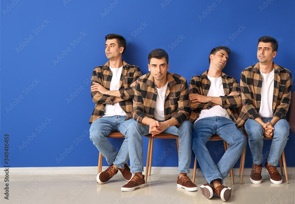 Waiting young men sitting on chairs near color wall