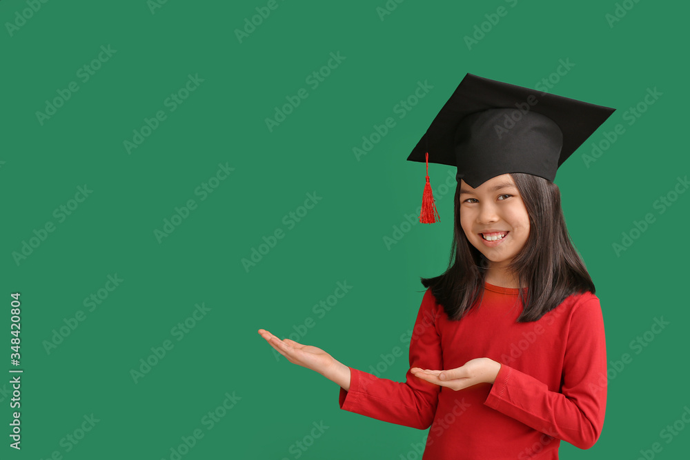 Little girl in graduation hat showing something on color background