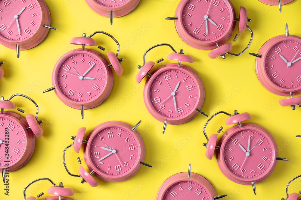 Creative layout of pink alarm clocks on pastel yellow background. Minimal concept.