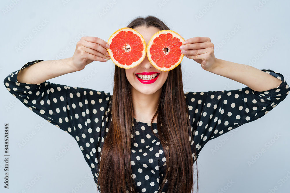 快乐的女孩把葡萄柚的两半举到眼睛附近。疯狂素食主义者的概念。面部表情