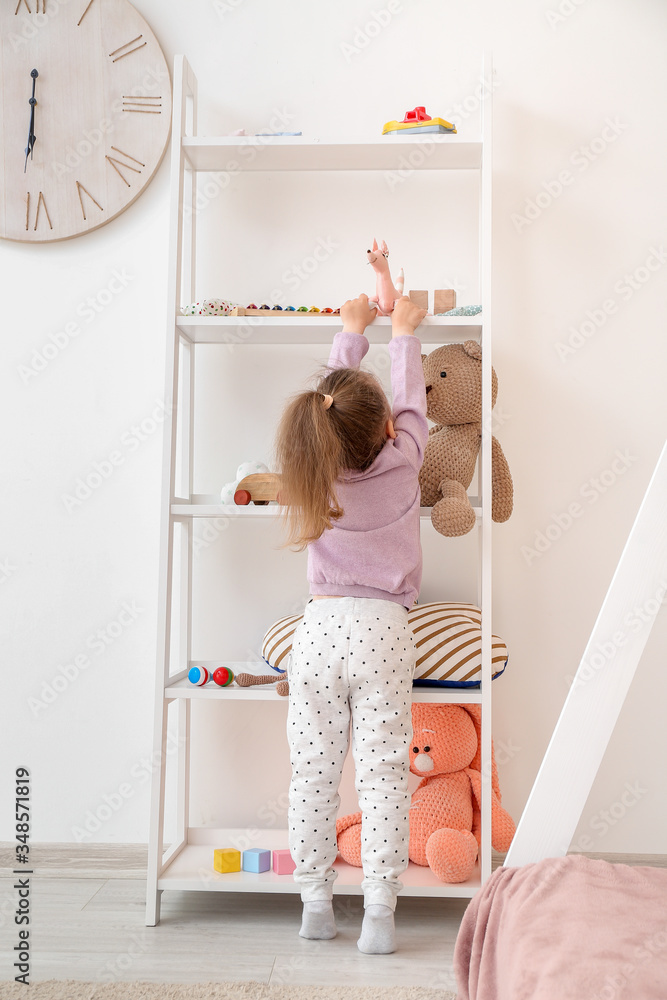 Little girl near rack with toys at home