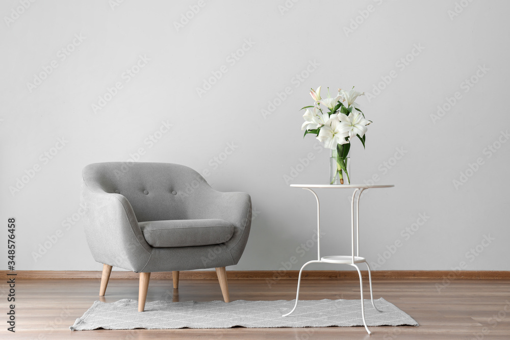 Comfortable armchair and table with lily flowers near grey wall in room