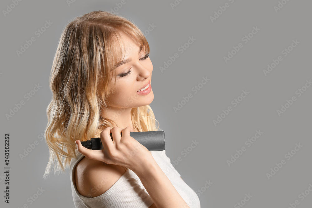 Beautiful young woman with hair spray on grey background