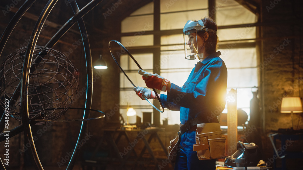 Young Contemporary Female Artist in Blue Jumpsuit and Safety Mask is Fitting a Metal Ring to a Tube 