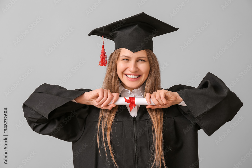 Female graduating student with diploma on light background