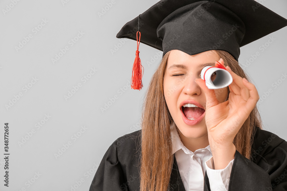 Female graduating student with diploma on light background