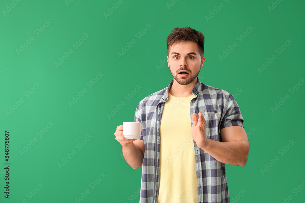 Shocked man with cup of hot coffee on color background