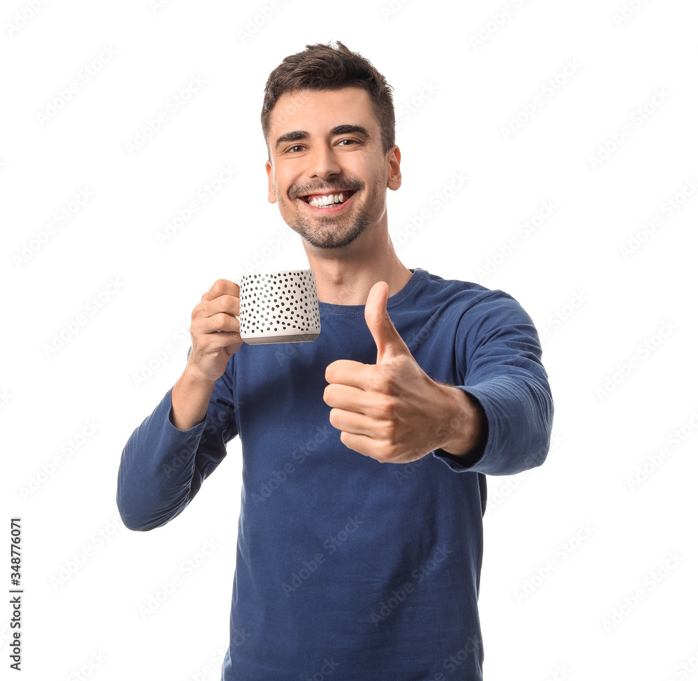 Young man with cup of hot coffee showing thumb-up on white background