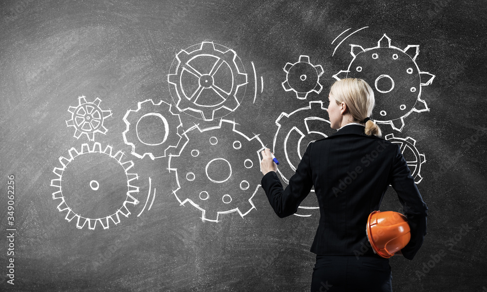 Businesswoman draws gears mechanism on blackboard