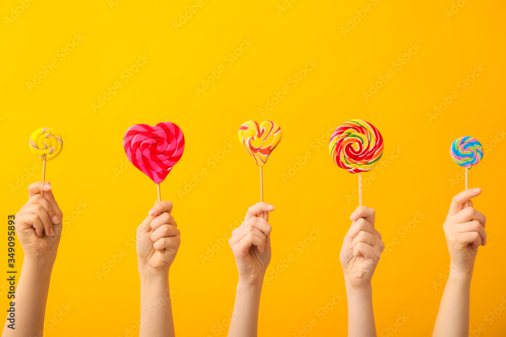 Hands with sweet lollipops on color background