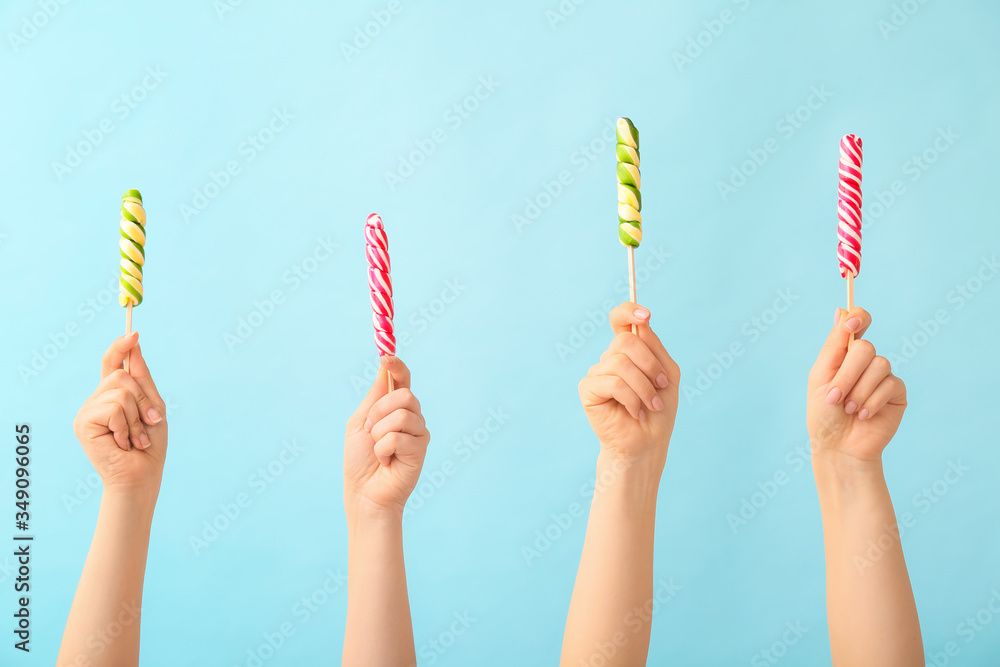 Hands with sweet lollipops on color background