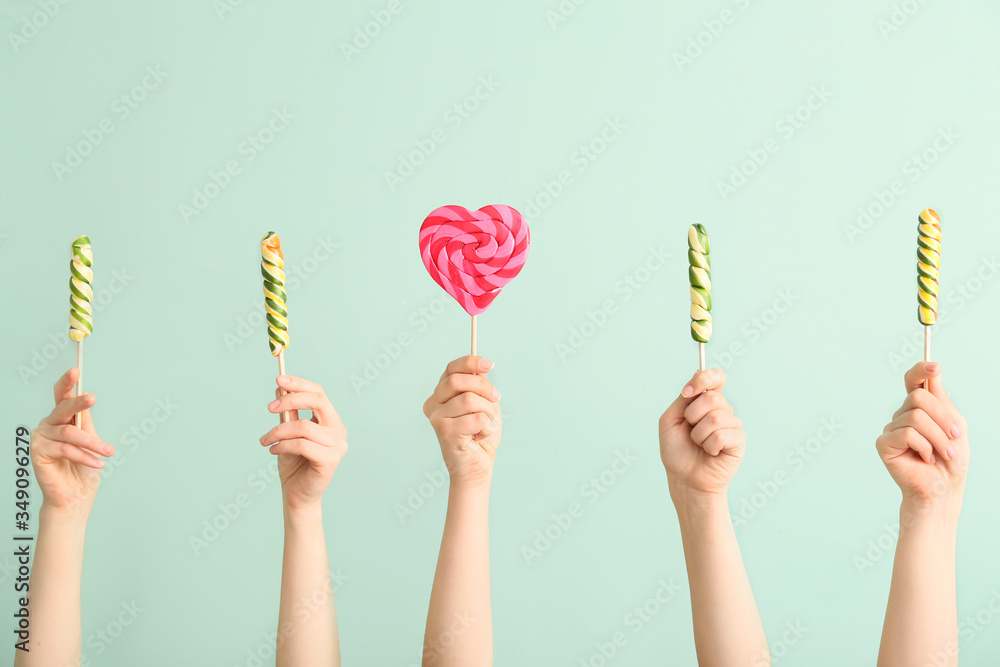 Hands with sweet lollipops on color background